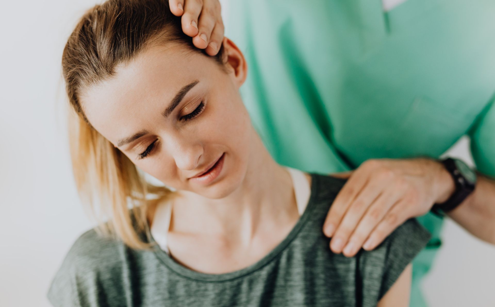 Crop professional male massage therapist in green medical uniform doing therapeutic neck massage on content female patient wearing casual clothes
